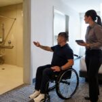 Wheelchair user and hotel staff verifying an accessible bedroom and roll-in shower