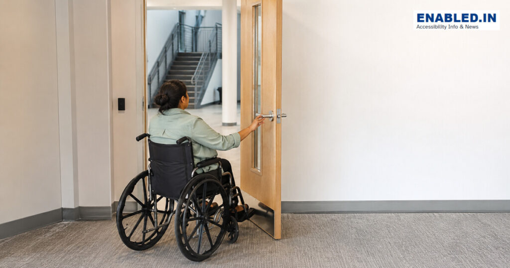 Wheelchair user independently operating a wide doorway with lever hardware, a vision panel and clear maneuvering space.