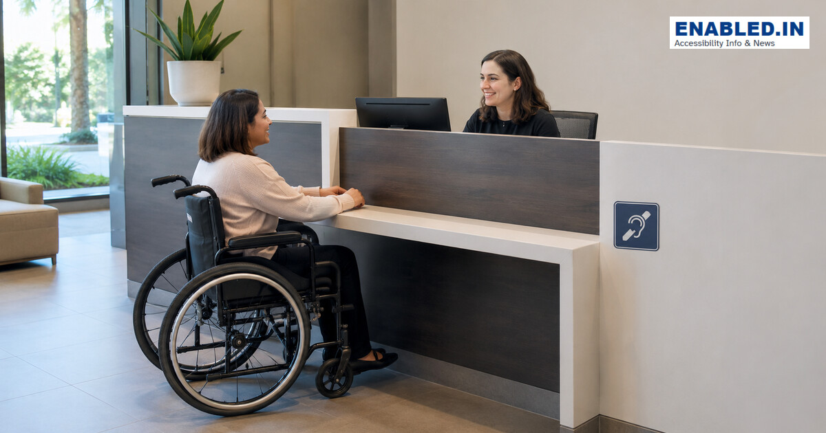 Wheelchair user speaking with a receptionist at a lowered counter with knee clearance.